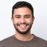 Young man dark hair smiling in front of white wall with brown shirt on